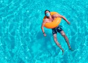man lays in pool in inner tube while wearing a mask amid coronavirus
