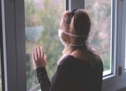 a white woman wearing a face mask stares out the window