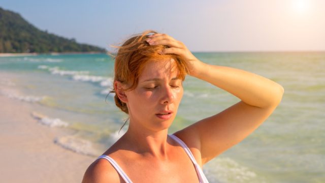 white woman sweating and putting her hand on her forehead on a sunny beach