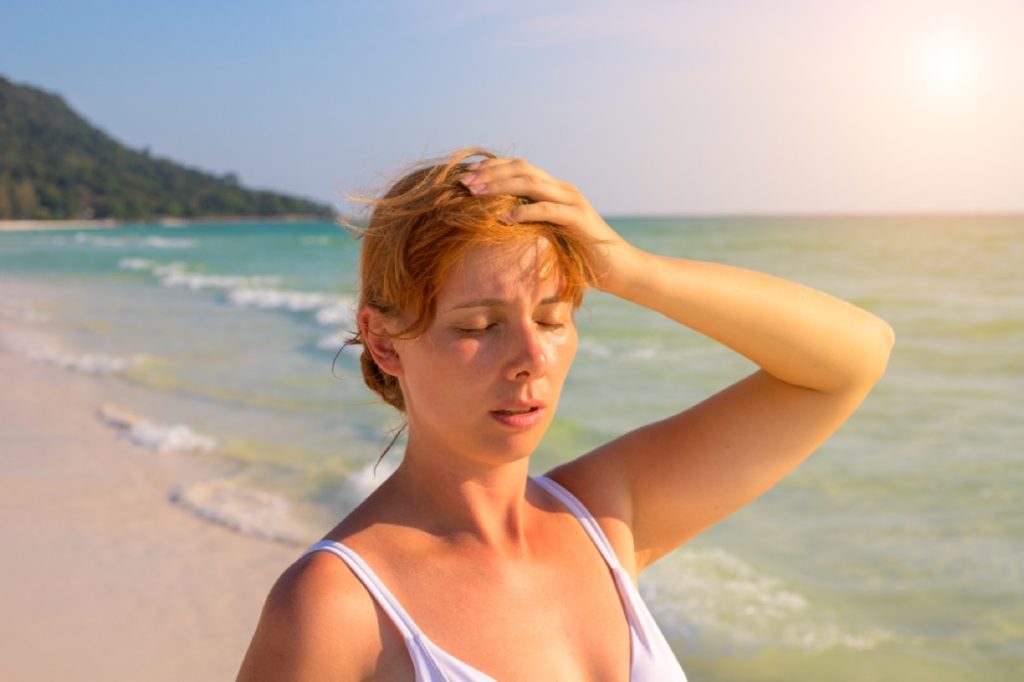 white woman sweating and putting her hand on her forehead on a sunny beach