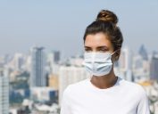 white woman with face mask standing on roof with city skyline in the background