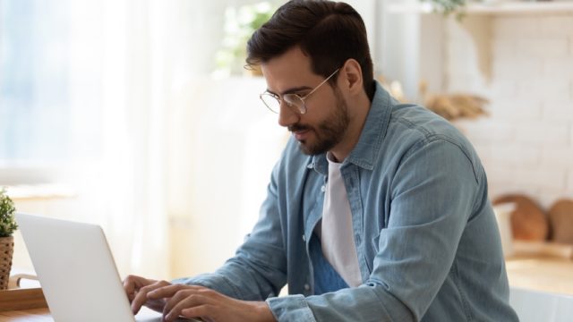 white man sitting and typing on his laptop while leaning forward
