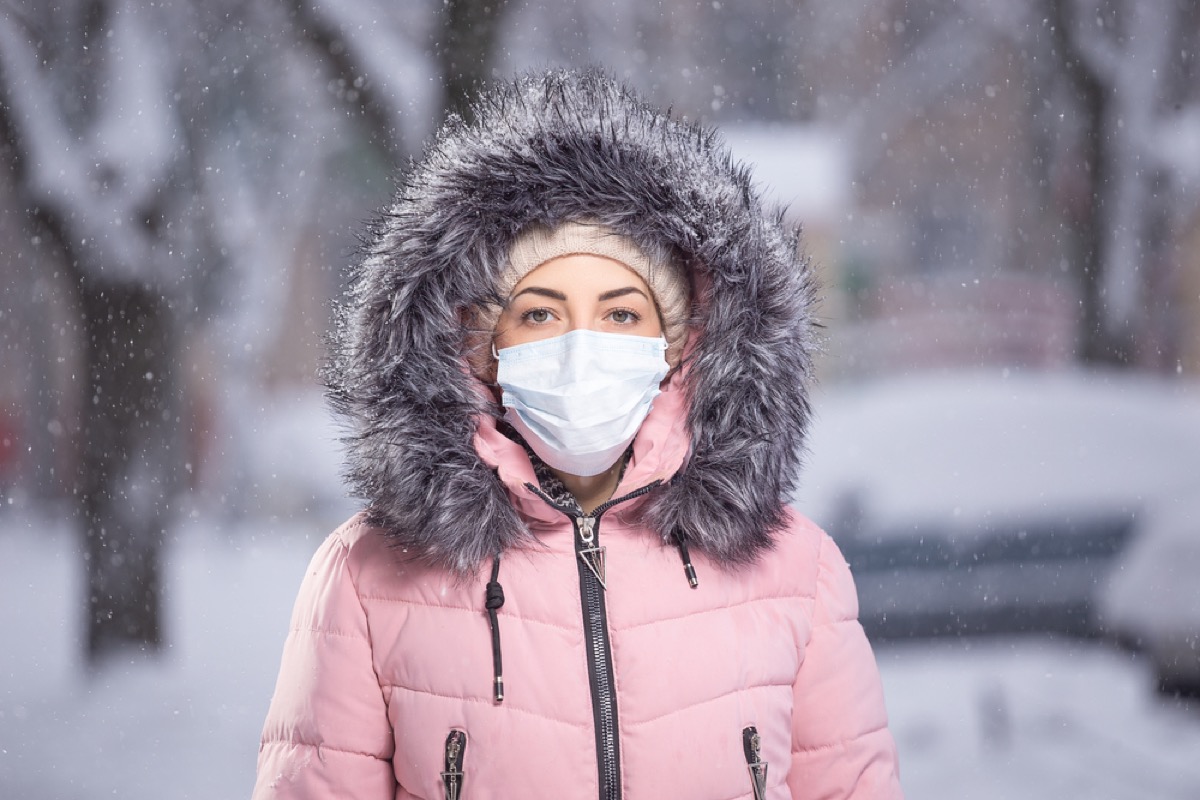 white woman in winter coat wearing a face mask in the snow