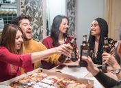 group of young people toasting beer and eating pizza