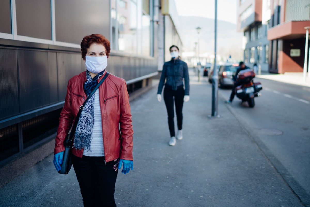 older woman with face mask walking on sidewalk with another woman walking behind