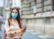 white woman with face mask and backpack holding phone outside
