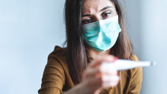 woman with face mask looking at thermometer