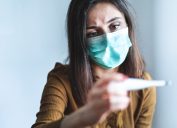 woman with face mask looking at thermometer