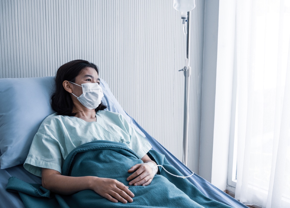 Woman with a face mask in a hospital bed looking out the window