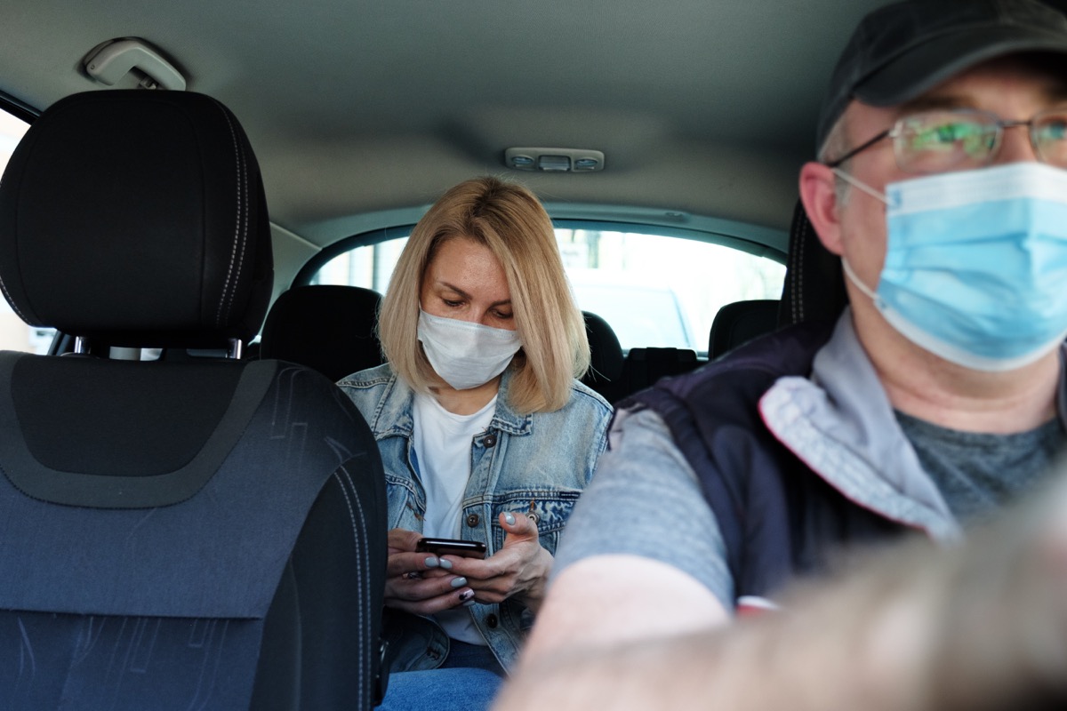 Woman in taxi wearing face mask for protection from pollution and viruses such as Coronavirus. Using smartphone