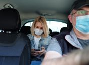 Woman in taxi wearing face mask for protection from pollution and viruses such as Coronavirus. Using smartphone