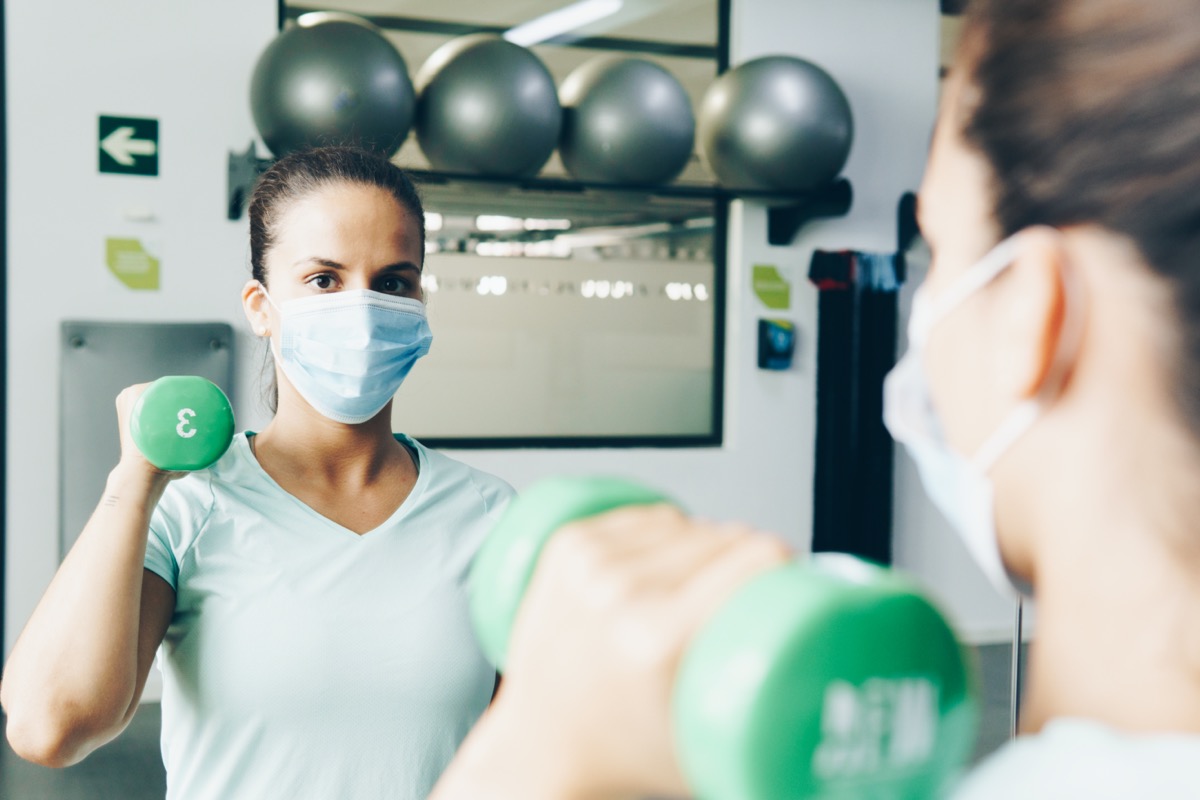 woman lifts gym weights in a gym with a mask on