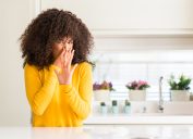 African american woman wearing yellow sweater at kitchen smelling something stinky and holding her nose