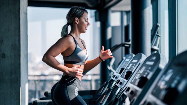 Side view of muscular woman running on treadmill.