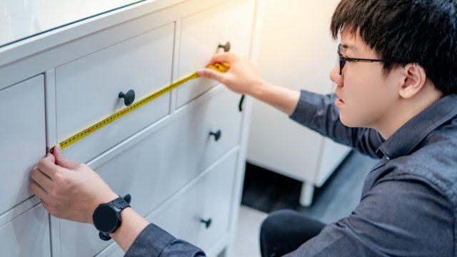 young asian man using tape measure to measure dresser