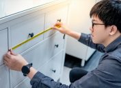 young asian man using tape measure to measure dresser