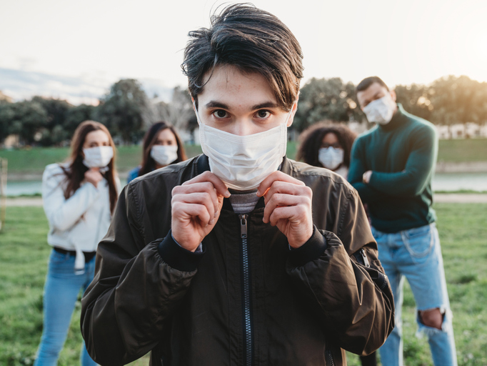 A young caucasian man wearing a face masks with a group of his friends standing behind him