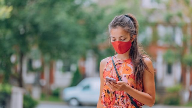 Asian woman in mask looking at phone for contact tracing