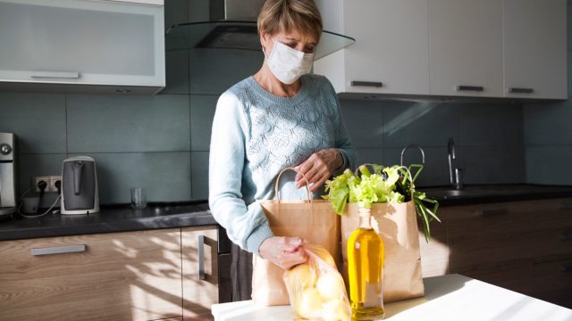 Older woman unpacking groceries with mask on