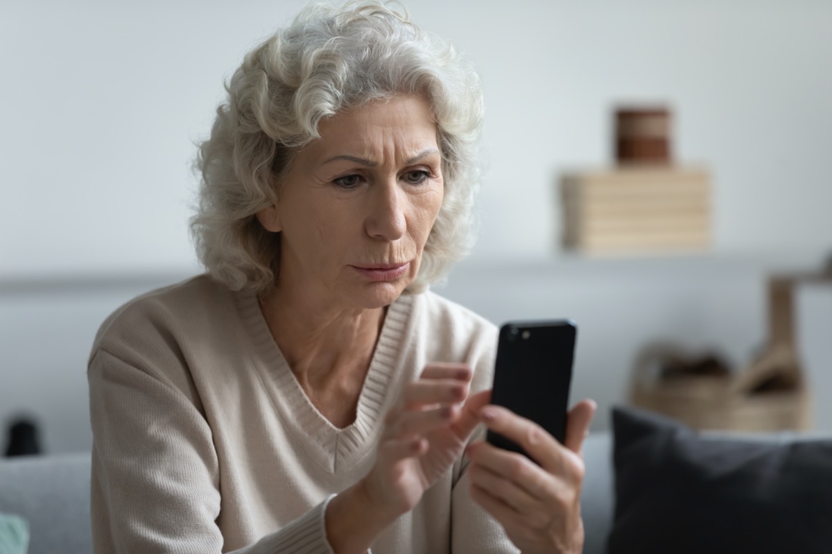 Senior whit woman looking at phone confused