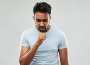 Young man coughing into fist