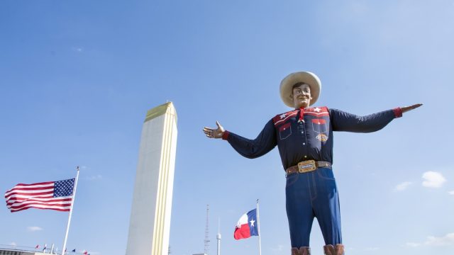 Dallas, Texas USA - October 11, 2015: Big Tex standing in front of the texas state flag and the american state flag waving at the entrance of the texas state fair. Big tex is the symbol of the fair and has been an icon not only of the fair, but dallas city for many years.