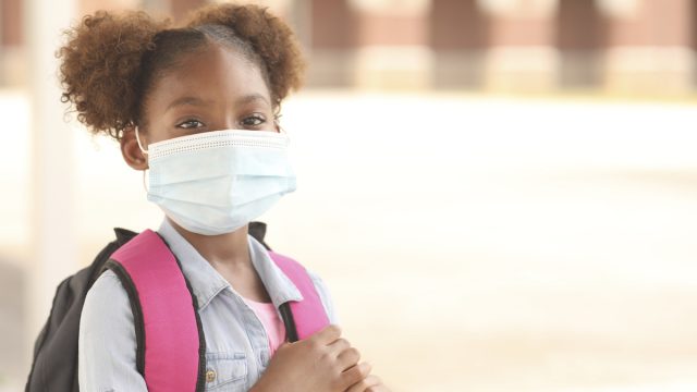 Black girl on school campus wearing a mask for coronavirus protection.