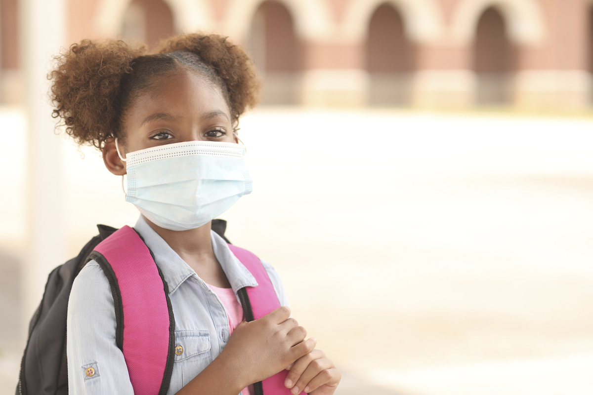 Black girl on school campus wearing a mask for coronavirus protection.