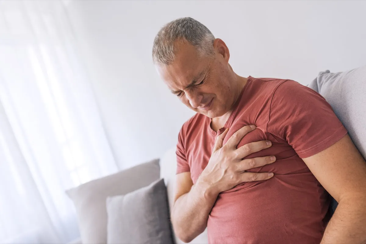 Severe heartache, man suffering from chest pain, having heart attack or painful cramps, pressing on chest with painful expression. Photo of Mature man suffering from chest pain at home during the day.