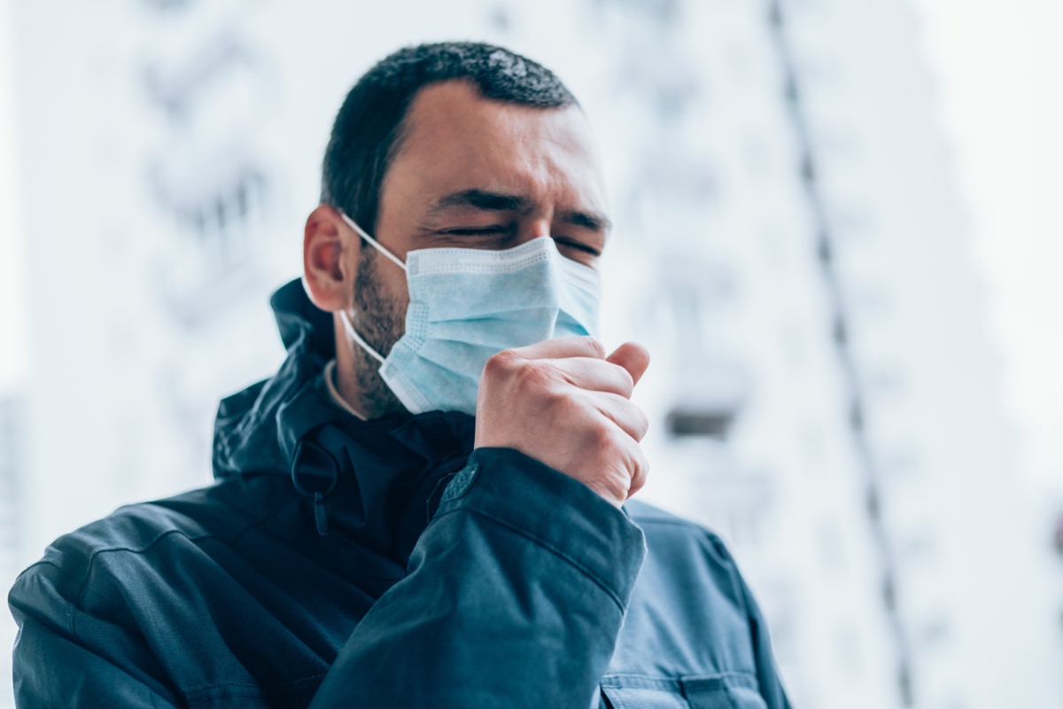 Young man wear face mask and coughing outdoors.