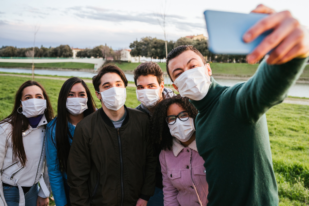 Group of teenage friends taking a selfie at park wearing protective masks