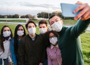 Group of teenage friends taking a selfie at park wearing protective masks