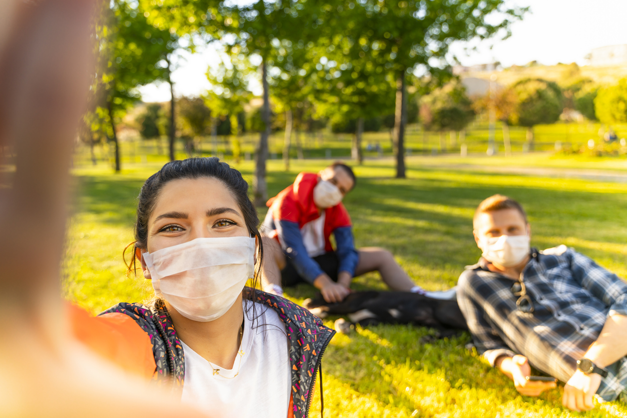 A group of young friends wearing face masks take a selfie in a park