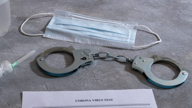 A pair of handcuffs and a face mask lie near a coronavirus test sheet