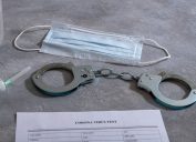 A pair of handcuffs and a face mask lie near a coronavirus test sheet