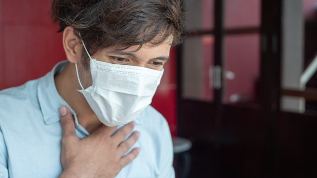 man in surgical mask grasping chest with breathing difficulties or asthma