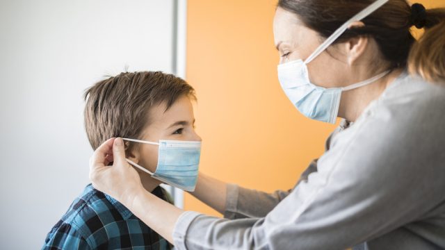 Adult woman putting on medical mask of little boy