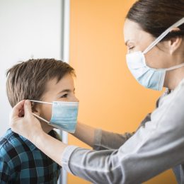 Adult woman putting on medical mask of little boy