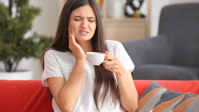 Girl experiencing mouth pain while drinking coffee