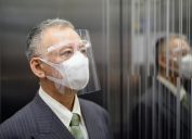 older asian businessman riding elevator while wearing face shield amid coronavirus