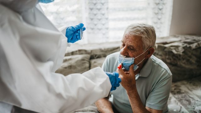 Doctor in protective suit taking nasal swab test from a senior man