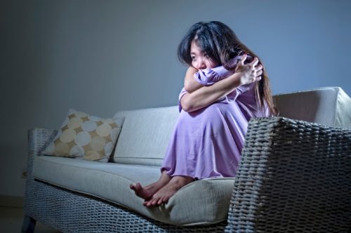 anxious asian woman clutching herself on the couch