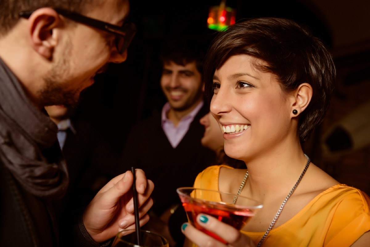 man talking closely to a woman at a bar holding a drink