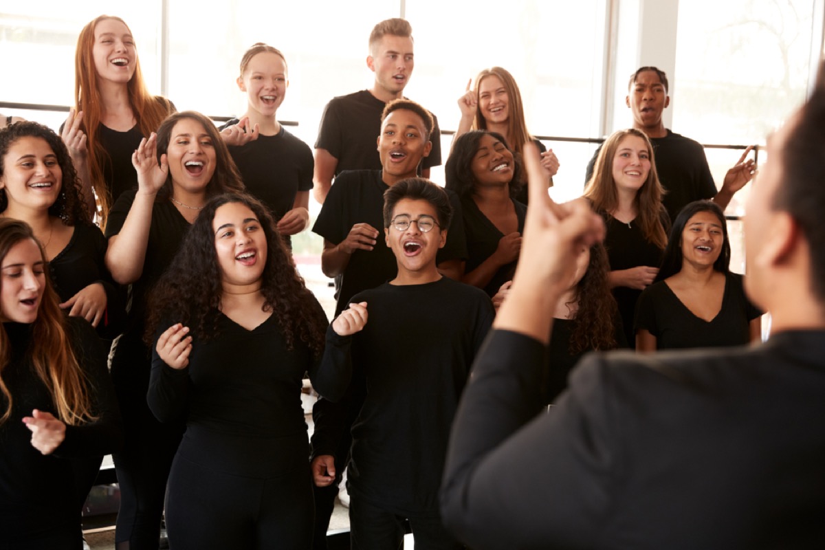 high school students singing in choir with teacher conducting