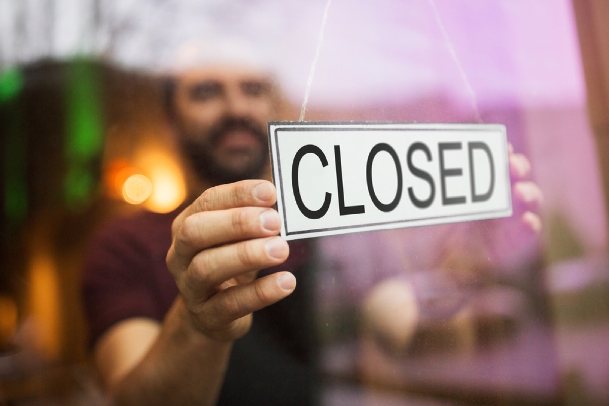 man putting closed sign in window