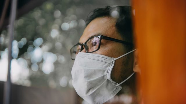 asian man with face mask looking out a window