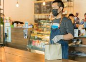 asian server wearing a face mask and gloves holding a bag at a cafe