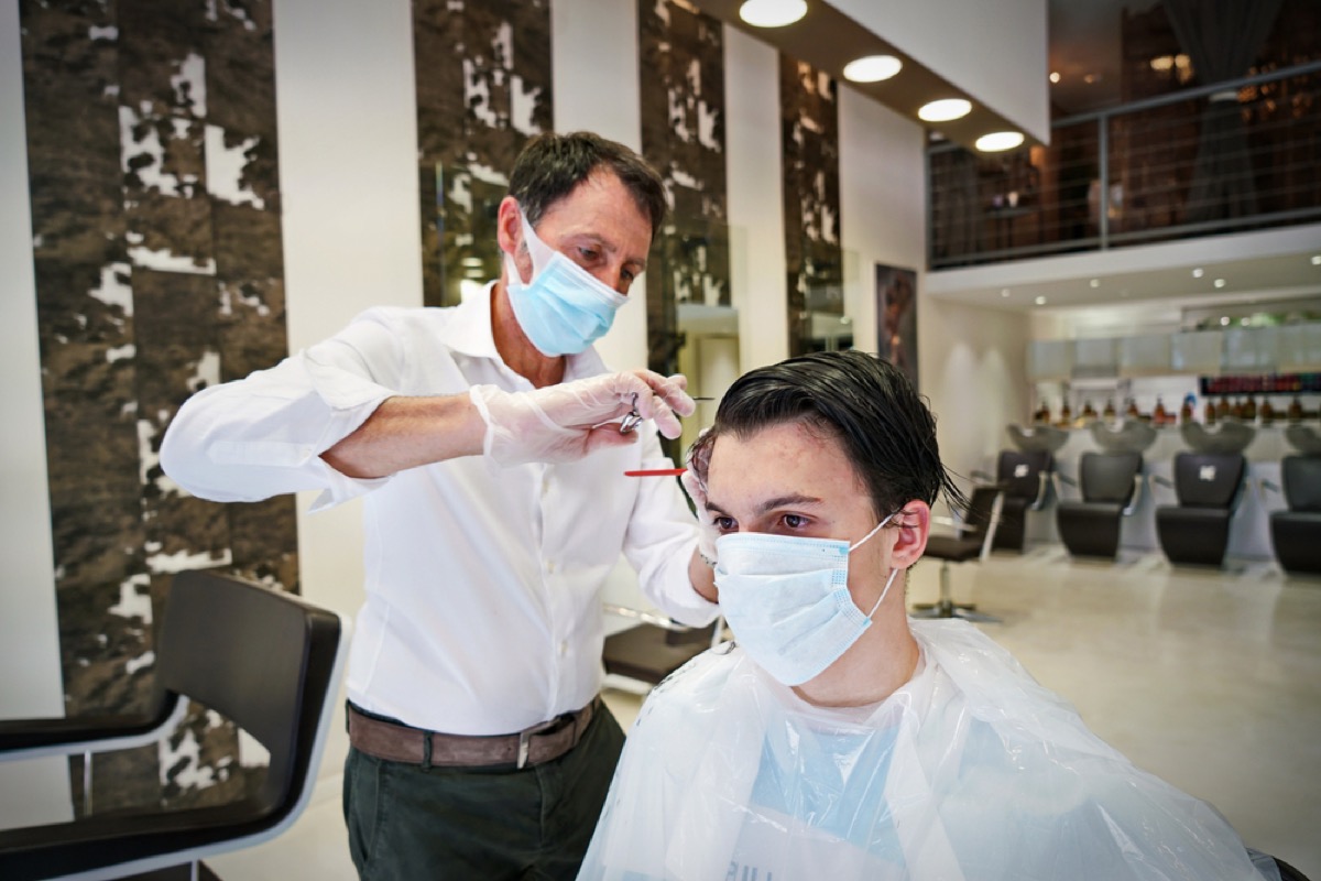 white barber with face mask cutting hair of white client with face mask
