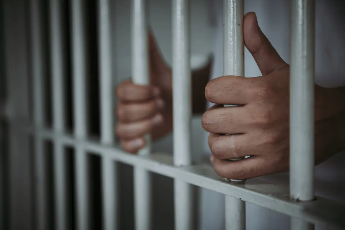 close up of hands holding bars in prison