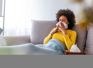 Woman on couch blowing nose sick at home